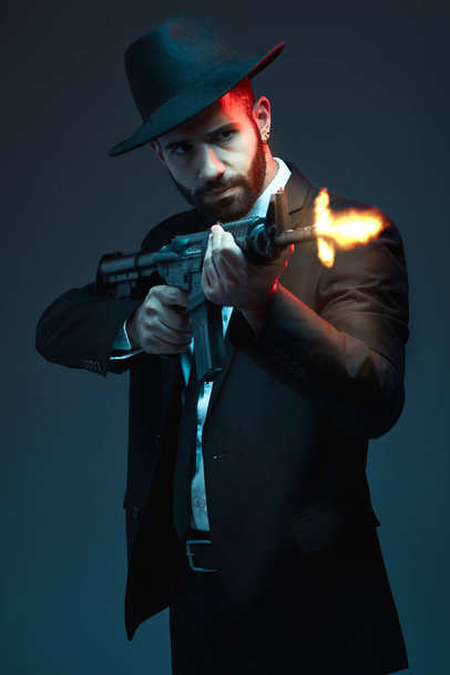 Man, suit or shooting gun on dark studio background in secret spy, isolated mafia leadership or crime lord security. Model, gangster or hitman firing gun in style, formal or fashion clothes aesthetic. - Photo, Image
