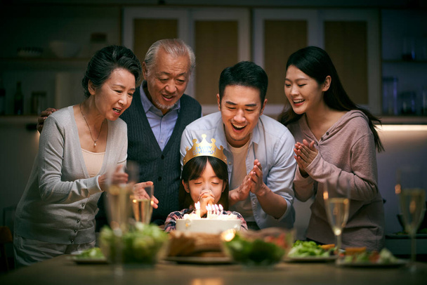 kleine asiatische Mädchen machen einen Wunsch, während drei Generation Familie ihren Geburtstag zu Hause feiert - Foto, Bild