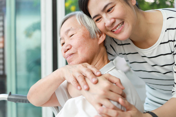 Счастливая женщина-сиделка обнимает пожилую женщину сзади с нежностью и любовью, азиатская взрослая дочь обняла ее тепло дома, время, проведенное вместе, семейное время, посещение пожилых людей, отношения - Фото, изображение