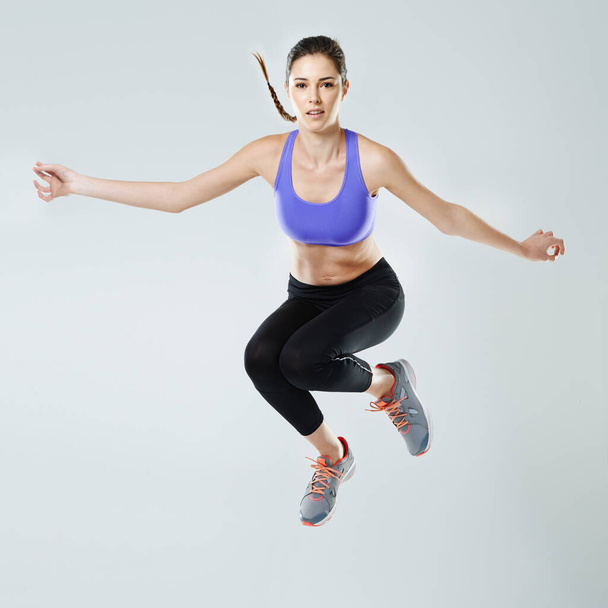 Er is geen limiet aan fitness. Een mooie jonge vrouw in sportkleding springt tegen een grijze achtergrond - Foto, afbeelding