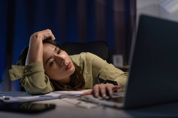 Ofis masasında laptopuyla çalışan uykulu, yorgun Asyalı genç iş kadını, gözleri kapanıyor. Fazla mesai konsepti - Fotoğraf, Görsel