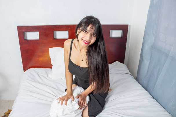 portrait of tender and sensual young mexican woman sitting on bed - Foto, imagen