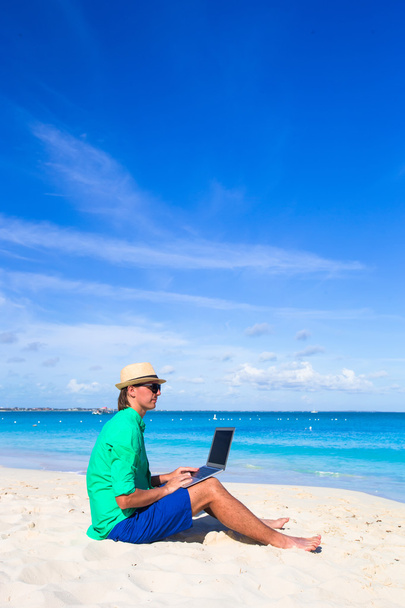 Молодой человек работает на ноутбуке на тропическом пляже
 - Фото, изображение