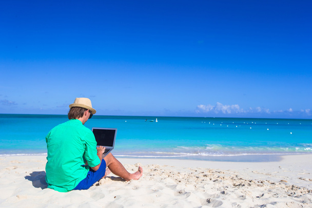 tropik sahilde dizüstü bilgisayarda çalışan genç adam - Fotoğraf, Görsel