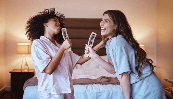 Friends, singing with brush and women in bedroom to get ready for girls night out dancing, fun music concert and happiness. Girl, friend and happy smile, girlfriends grooming at sleepover in pajamas - 写真・画像