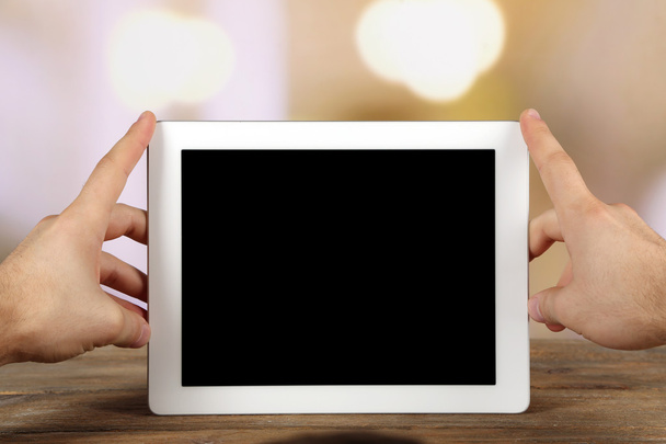Hands holding tablet PC on wooden table and light blurred background - Photo, Image