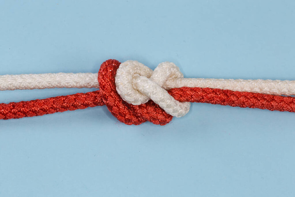 Tightened rope sliding figures of eight knot, also known as double figure-eight bend, used for connecting of two ropes of the same diameter, view on a blue background close-up - Photo, Image