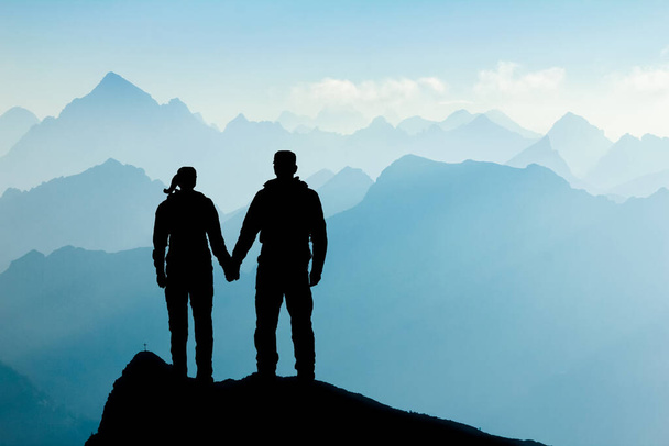 Влюбленная пара, стоящая на вершине горы, держась за руки. Мужчина и женщина наслаждаются восходом солнца после успешного похода на вершину горы. Тироль, Австрия. Аллен, Бавария. - Фото, изображение
