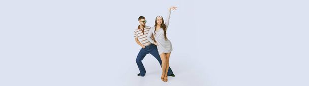 Young beautiful girl in silver dress and stylish man dancing disco dance isolated over grey studio background. 70s fashion, hobby, hippie lifestyle, American culture. Copy space for ad, text. Banner - Foto, imagen