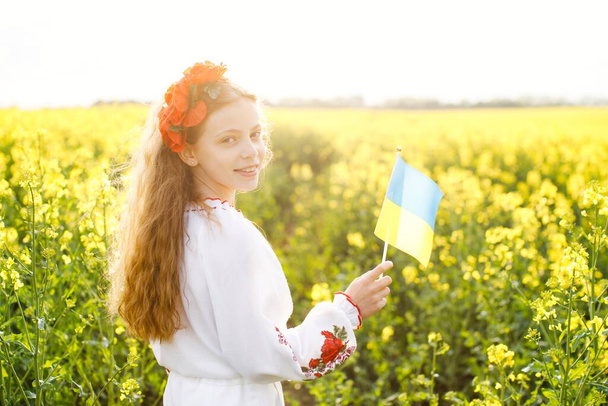 Pray for Ukraine. Child with Ukrainian flag in rapeseed field. Little girl holding national flag in her hand. - Foto, imagen