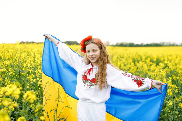 Pray for Ukraine. Child with Ukrainian flag in rapeseed field. Girl holding national flag praying for peace. - Foto, Imagem