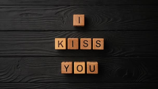 Drewniane kostki stop-motion ze zwrotem I Kiss You na czarnym tle - drewniany stół. Słowa pocałunku są zrobione z liter z drewna dla twojej dziewczyny, chłopaka, żony, męża, dla Walentynek - Materiał filmowy, wideo