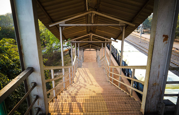 Vasútállomás láb a lépcsőház felett megy Foot át híd, belülről kilátás állomás folyosó, lépcső egy láb át a hídon egy vidéki vasútállomáson, és napsugár jön a bal oldalról - Fotó, kép