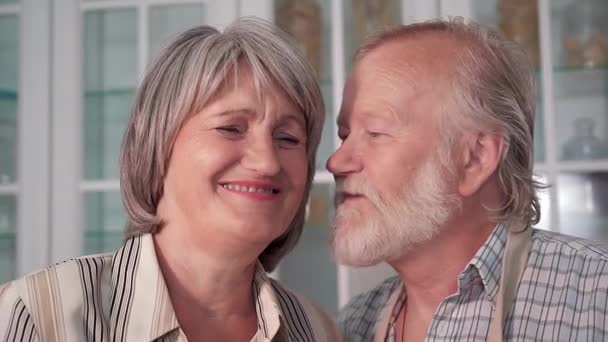 portret starszej pary, starszy mężczyzna całuje żonę w policzek, uśmiecha się i patrzy w kamerę - Materiał filmowy, wideo