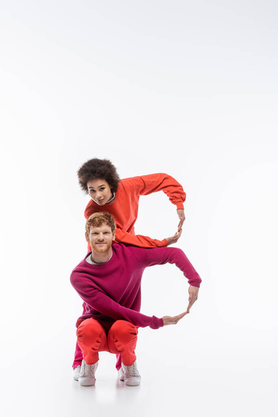 cheerful interracial couple in magenta color clothes showing b letter with hands on white background  - Foto, Imagen
