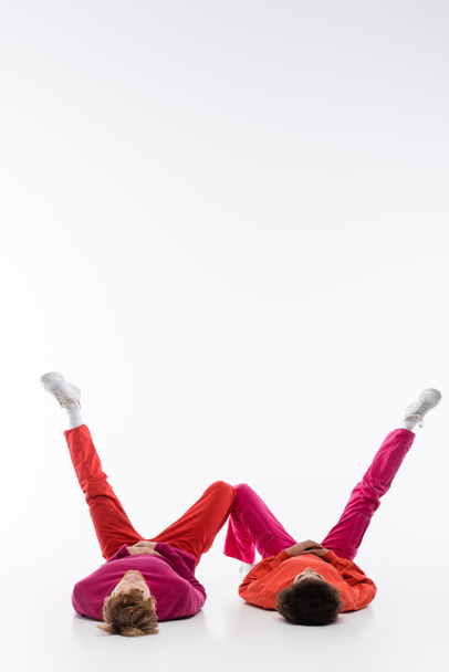 межрасовая пара в пурпурной одежде цвета лежа на полу и показывая букву с ногами на белом фоне  - Фото, изображение