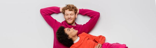 top view of happy african american woman resting with redhead man in magenta color clothes on white, banner  - Valokuva, kuva