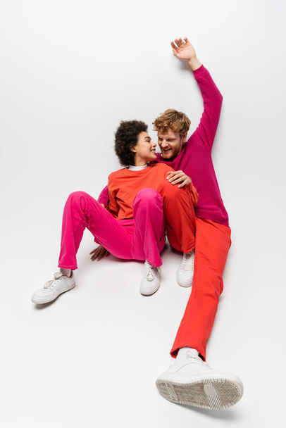 positive african american woman sitting with happy man in magenta color clothes raising hand on white  - Foto, immagini