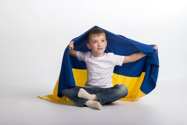 a little boy is sitting on the floor and holding the flag of Ukraine - Photo, Image