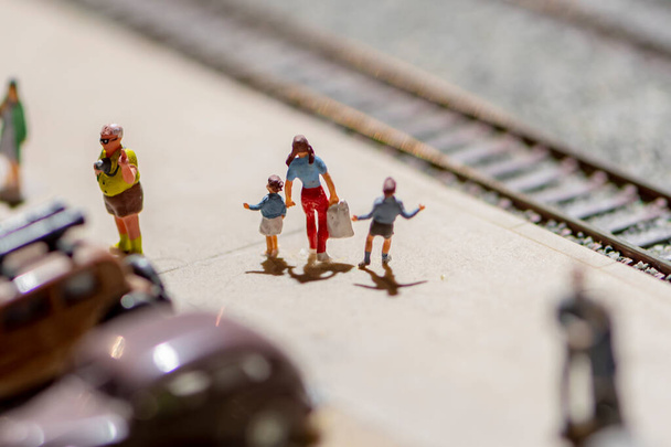 Игрушечные фигурки людей на платформе железнодорожного вокзала, парковка для автомобилей, железнодорожные рельсы. - Фото, изображение