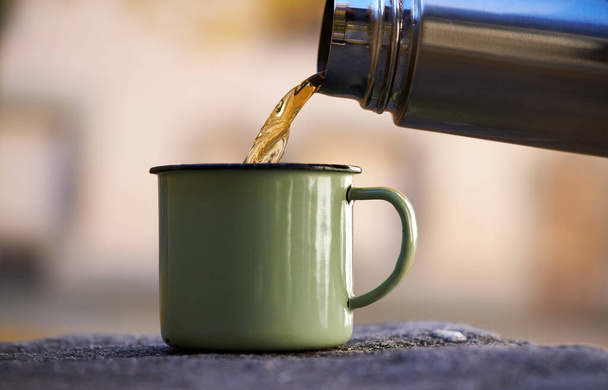 Налить теплый чай из вакуумной бутылки в металлическую чашку во время туристической поездки - Фото, изображение