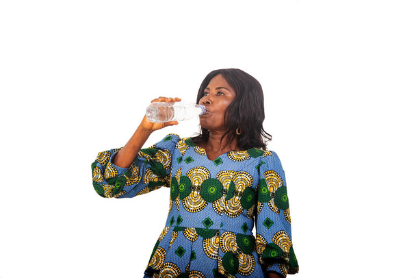 mooie zakenvrouw in traditionele kleren staan op witte achtergrond drinkwater uit een fles. - Foto, afbeelding