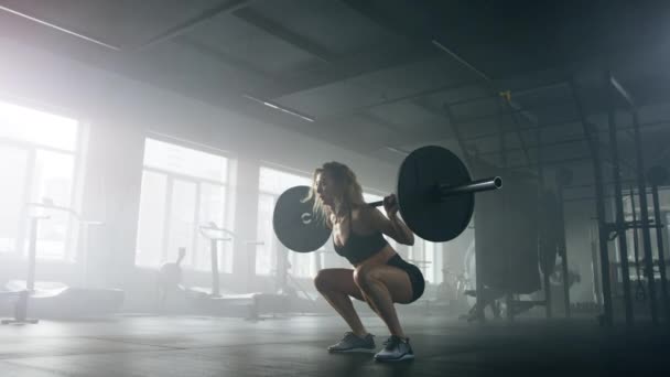 Vista de cerca del levantador de pesas femenino durante un entrenamiento con barra en un moderno y oscuro estudio de gimnasia. Joven deportista caucásica en cuclillas con pesas pesadas en interiores. Imágenes de alta calidad 4k - Metraje, vídeo