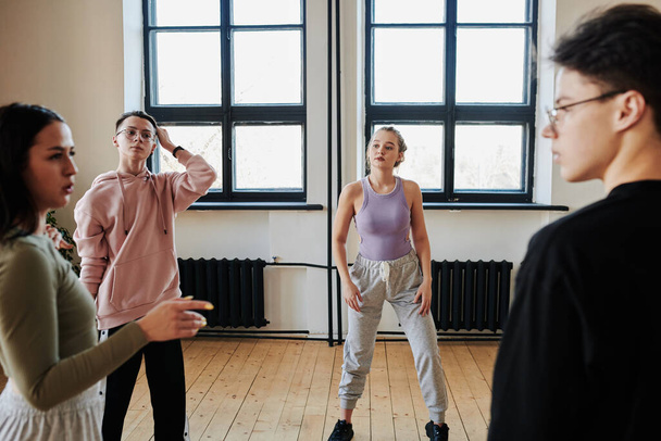 Teenage guys and girls in activewear discussing difficulties of new movements at break after hard training in studio or dance hall - Foto, afbeelding