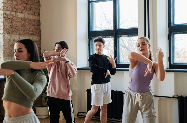Young male instructor of vogue dancing group consulting teenage girls and guy in activewear repeating new movement at training - Foto, Bild