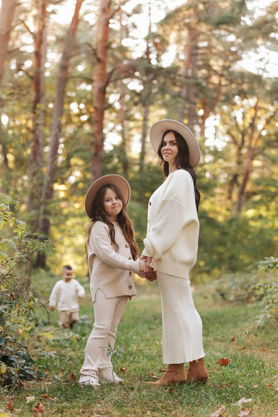 Beautiful smiling young mother with teen daughter are holding hands and walking outdoors in the autumn park. Mothers day. Family day. Idyllic stylish family of two communicate alone. happy childhood - Photo, image
