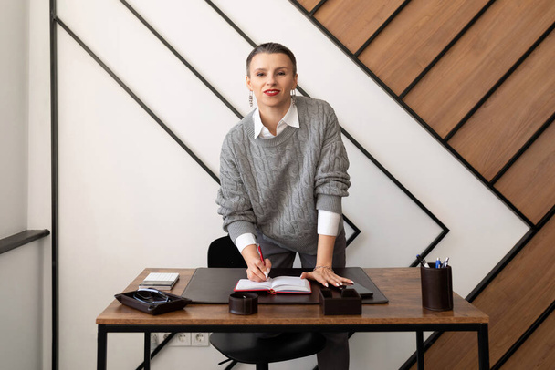 Geschäftsfrau mit Kurzhaarschnitt im grauen Pullover am Schreibtisch im Büro. - Foto, Bild