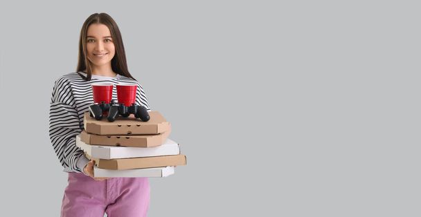 Young woman with boxes of tasty pizza, game pads and drinks on grey background with space for text - Foto, imagen