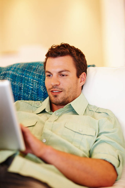 Uwielbiam mojego nowego e-czytnika. Przystojny mężczyzna relaksujący się na kanapie pracujący na tablecie cyfrowym - Zdjęcie, obraz