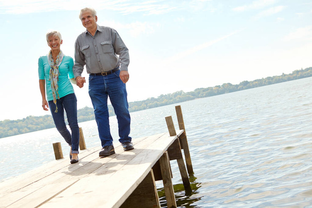 質の高い時間を一緒に過ごす。一緒に桟橋に沿って歩いている高齢者のカップル - 写真・画像