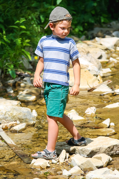 El niño juega cerca de un arroyo de montaña
 - Foto, Imagen