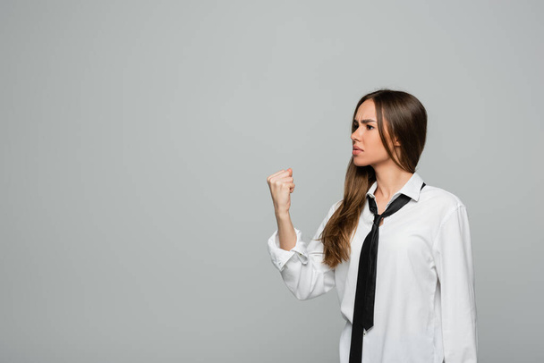 angry young woman in white shirt and tie showing clenched fist isolated on grey - Foto, Imagem
