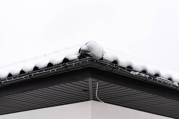 The roof of a single-family house is covered with snow against a cloudy sky, visible ridge tile on the roof and falling snow. - Photo, image