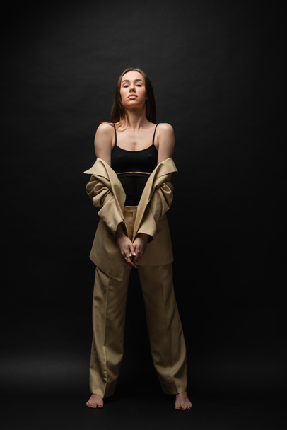 full length of barefoot young woman in beige suit standing on black  - Fotografie, Obrázek