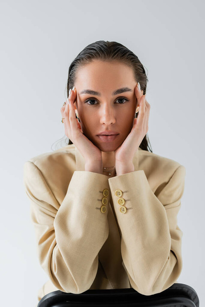joli modèle en blazer élégant beige regardant la caméra isolée sur gris  - Photo, image