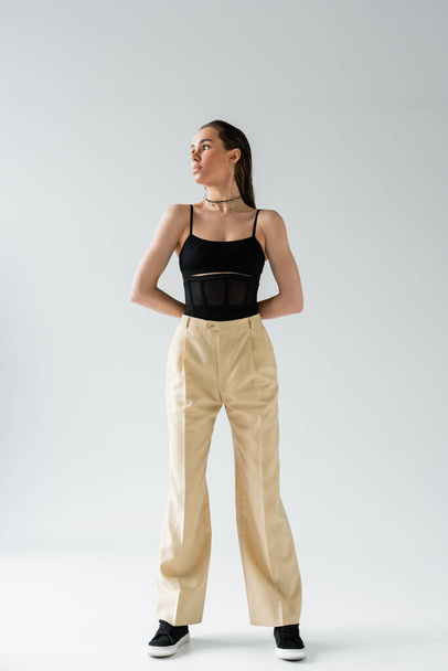 full length of pretty model in beige pants and black top looking away on grey  - Photo, Image