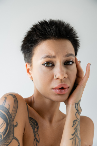 portré feldúlt tetovált nő smink és piercing megható arc és nézi kamera elszigetelt szürke - Fotó, kép