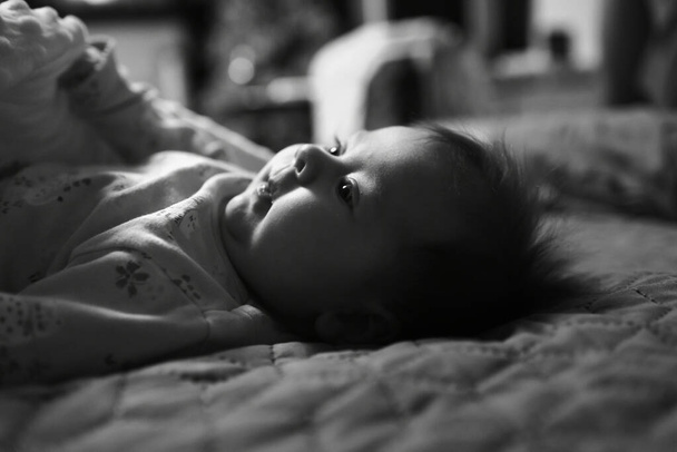 Baby lies in bed with open eyes. Baby woke up. Black and white  - Fotografie, Obrázek