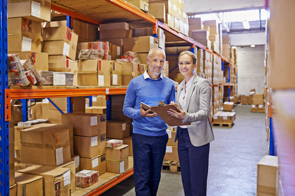 We take the guess work out of shipping. Portrait of a man and woman inspecting inventory in a large distribution warehouse - Foto, Imagen