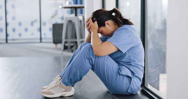 Healthcare, stress and sad nurse on floor with burnout, anxiety and headache working in emergency services. Medical care, mental health and health care worker with depression in hospital or clinic. - Photo, Image