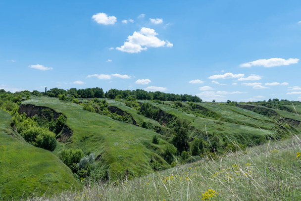 View ravine covered with greenery. Landscape valley with geological faults. Earthen mountains and bumps relief on against sky. Hill beam with protrusions and recesses. Grass and trees on slope canyon. - Valokuva, kuva