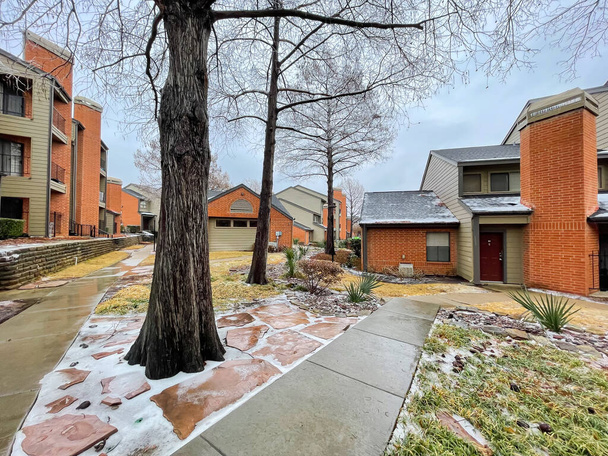 High terrain wall along concrete pathway with snow and ice covered at apartment complex near Dallas, Texas, America after winter storm. Rental buildings townhome with shingle rooftop, cedar trees - Zdjęcie, obraz