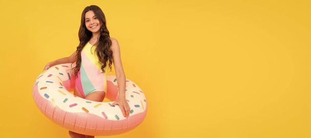 happy kid in swimming suit with doughnut inflatable ring on yellow background. Banner of summer child girl in swimsuit, studio poster header with copy space - Foto, immagini