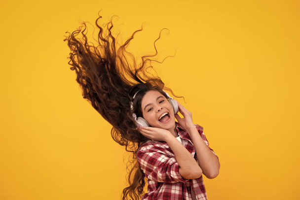 Teenager child girl in headphones listening music, wearing stylish casual outfit isolated over yellow background. Happy teenager with earphones, positive and smiling emotions of teen girl - Photo, image