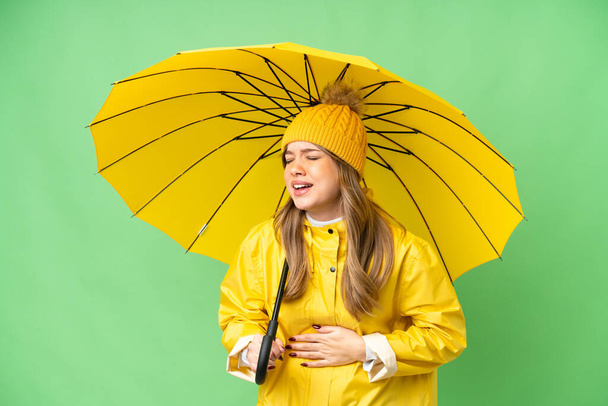 Молода дівчина з дощовим пальто і парасолькою над ізольованим ключовим фоном хромосоми, багато посміхаючись
 - Фото, зображення