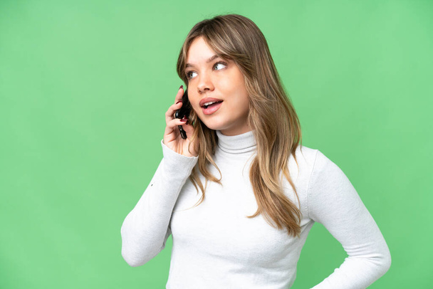 Young girl over isolated chroma key background keeping a conversation with the mobile phone with someone - Foto, Imagem
